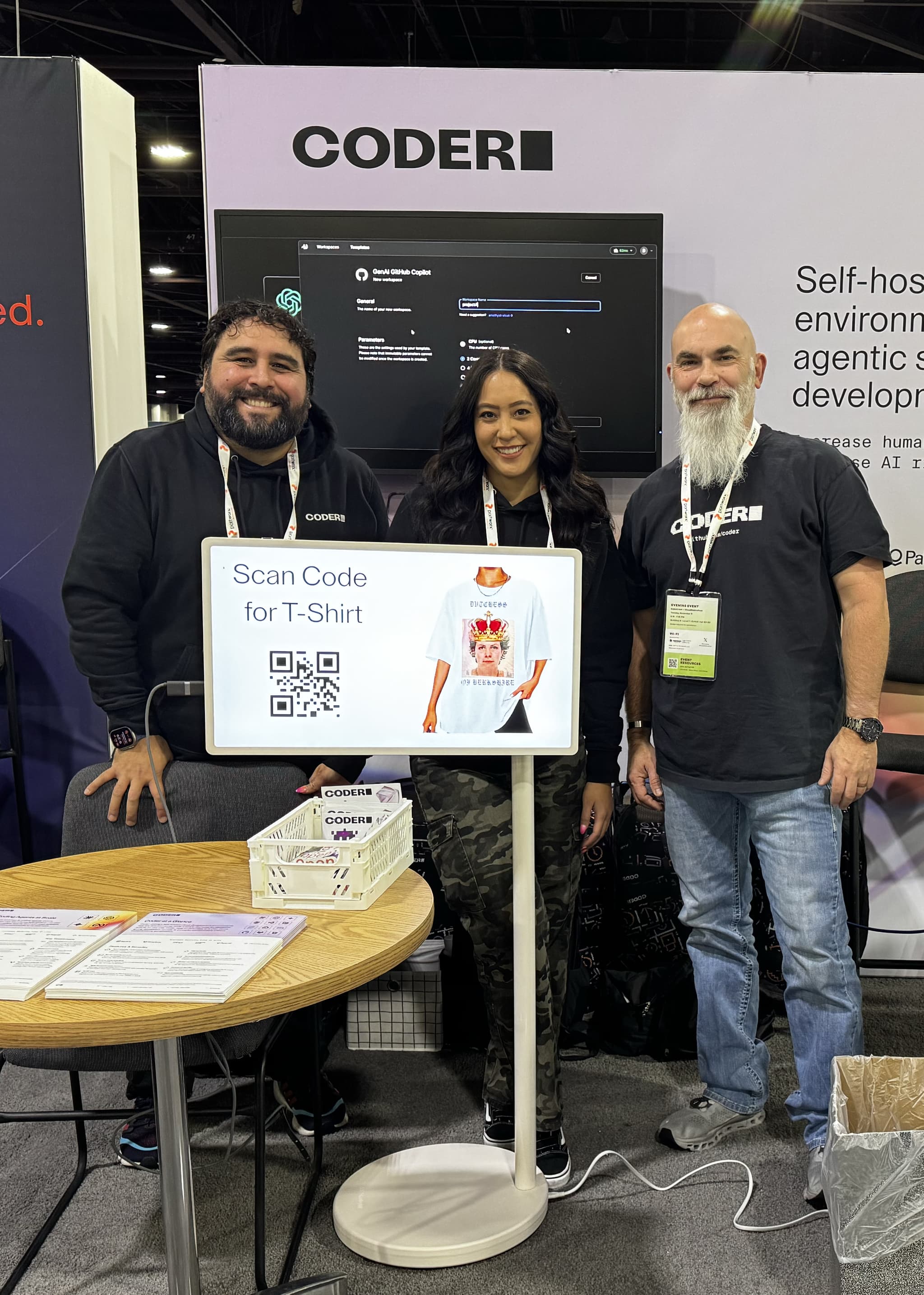3 people in Coder shirts smiling in front of a backdrop with the Coder logo and a screenshot of a Coder workspace