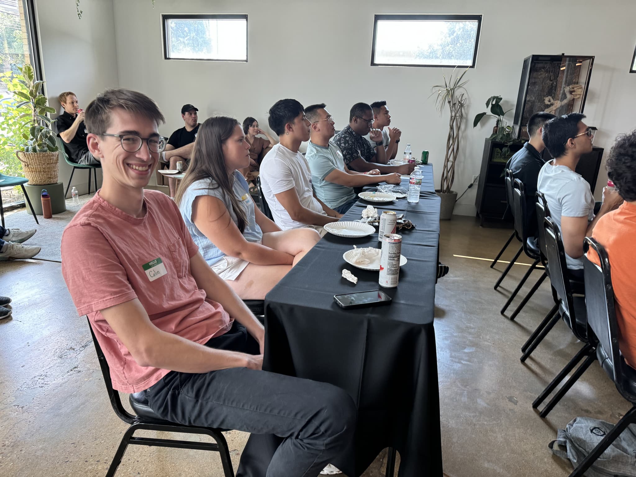person smiling at the viewer while seated in a row of people listening to a conference talk
