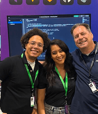 3 people with conference lanyards smiling in front of a code editor