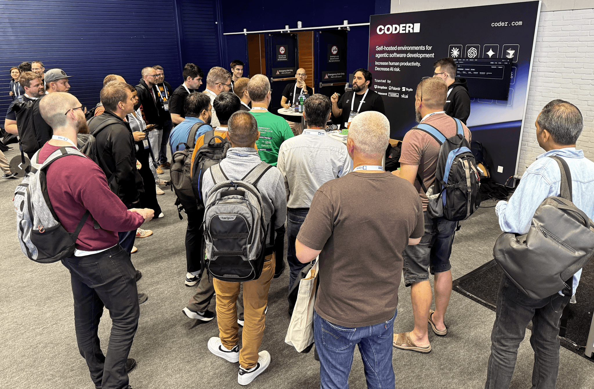 small crowd of people gathered around a Coder conference booth as a person wearing a Coder lanyard addresses them