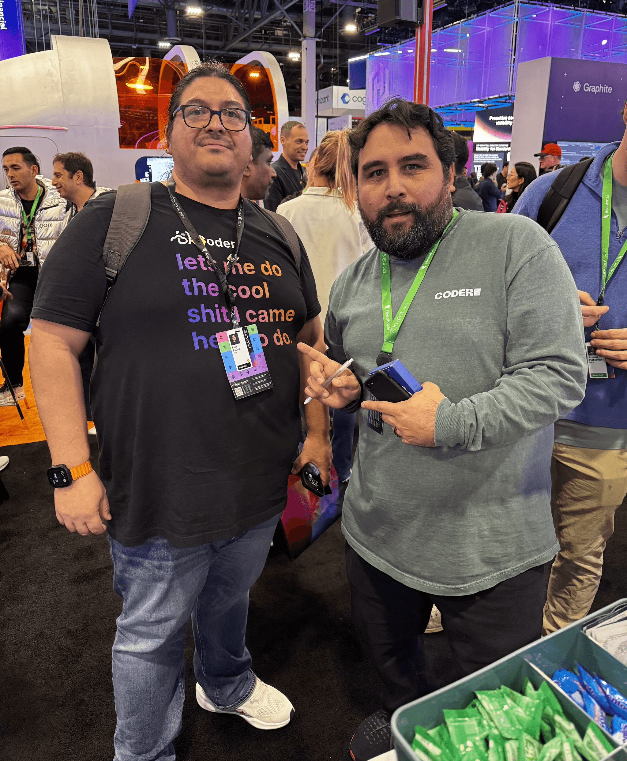 2 people wearing lanyards over Coder shirts standing in a packed conference hall