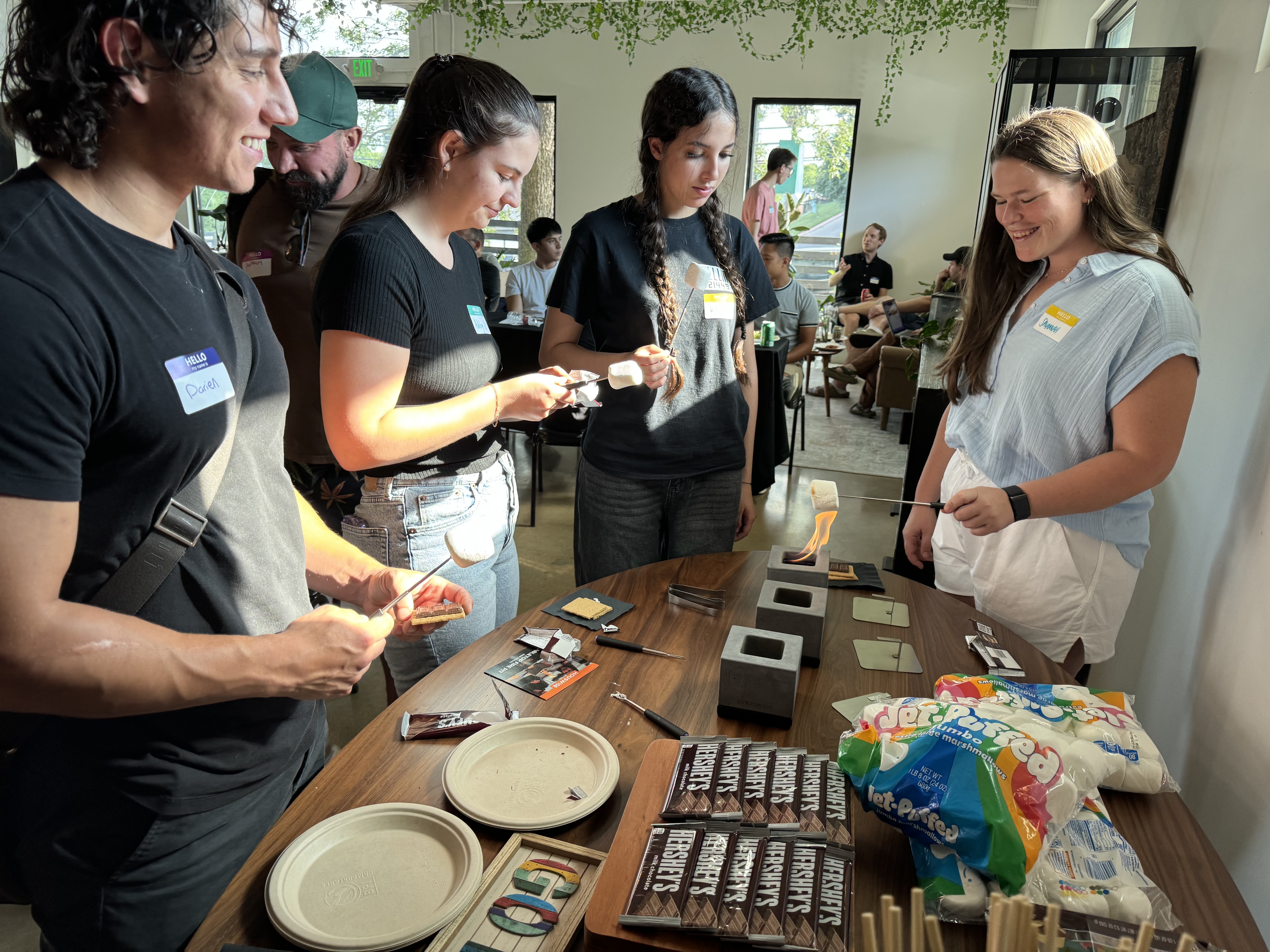 4 people making s'mores indoors with small portable fire pits on top of a table