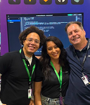 3 people with conference lanyards smiling in front of a code editor