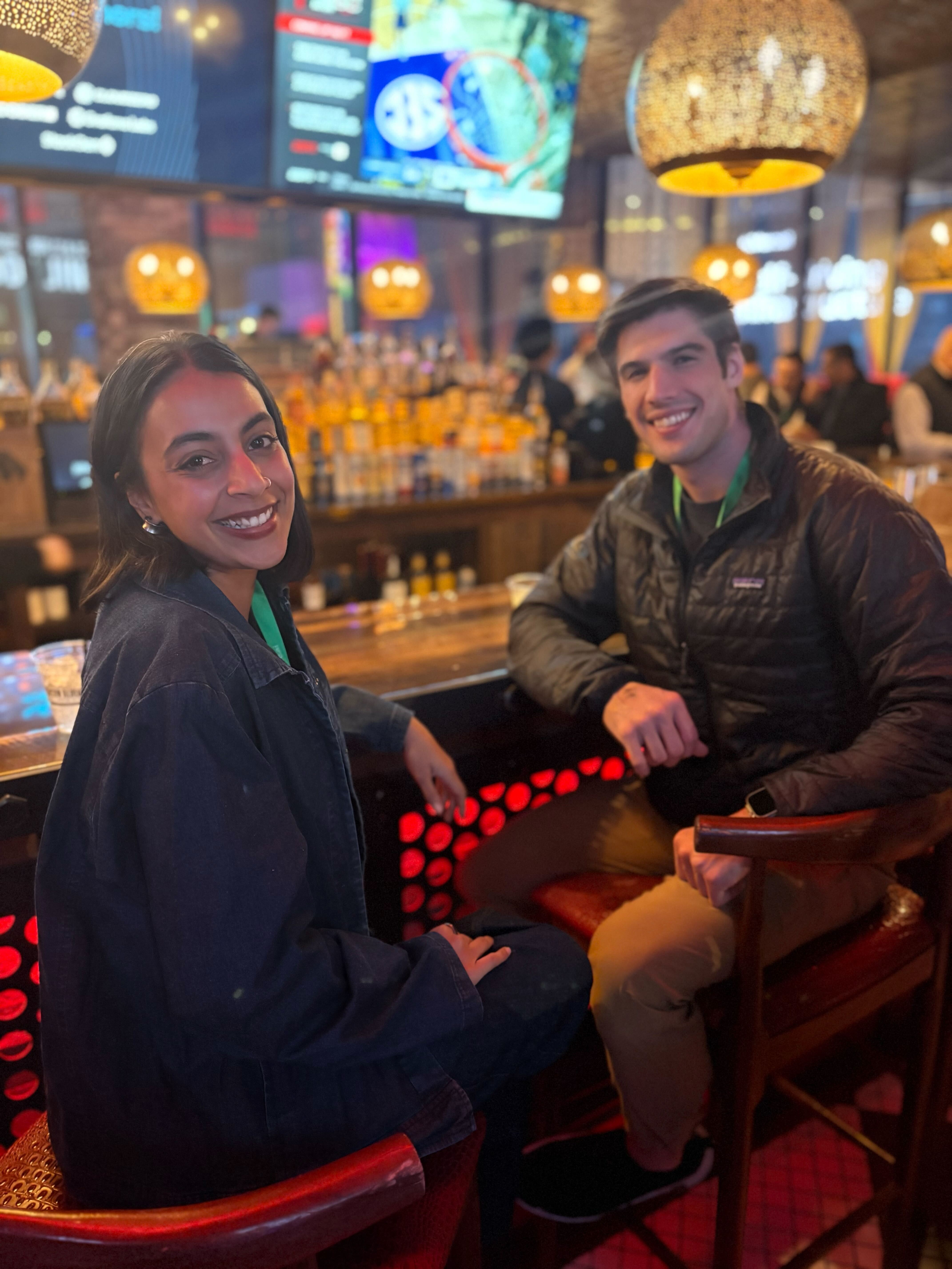 2 people smiling while seated at a colorful bar